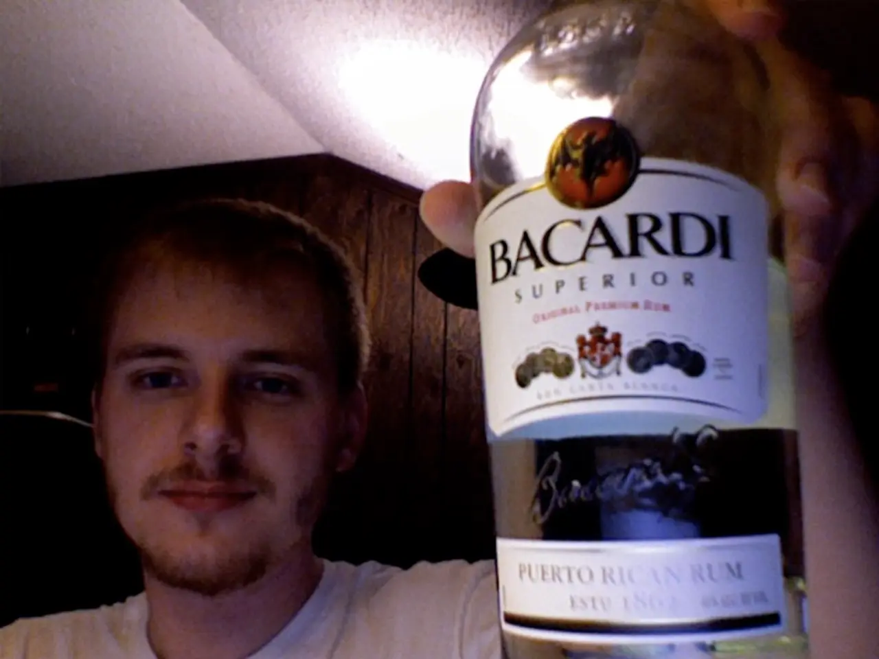 In this image a person wearing a white shirt is holding a bottle labelled as bacardi superior.
