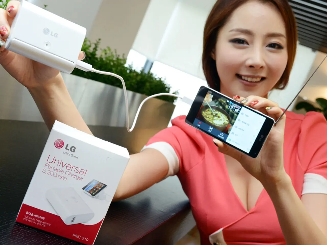 This is the woman standing and smiling. She is holding a mobile phone, which is connected to a...