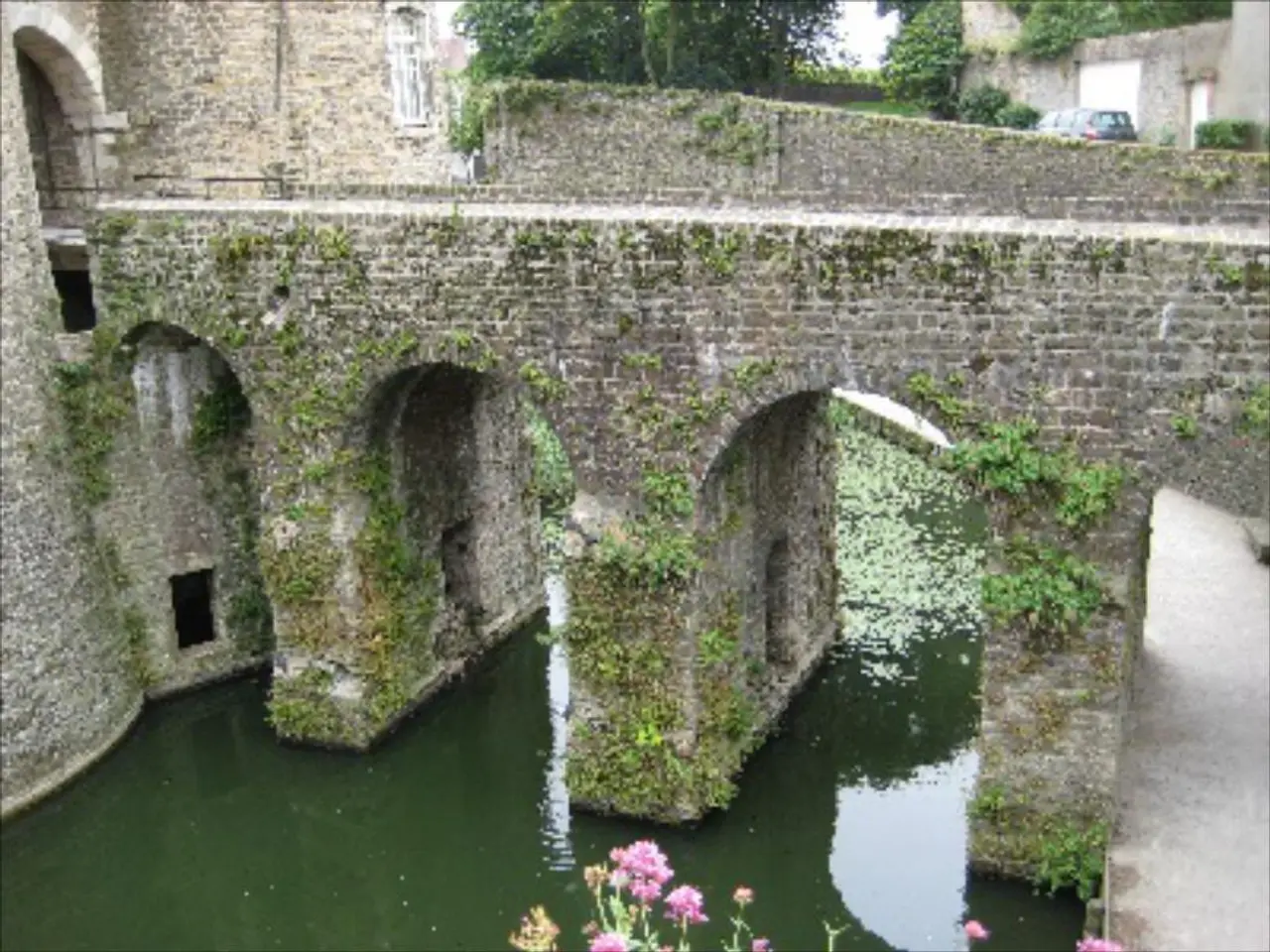 In the center of the image we can see a bridge. At the bottom there is a road, tree and water. At...