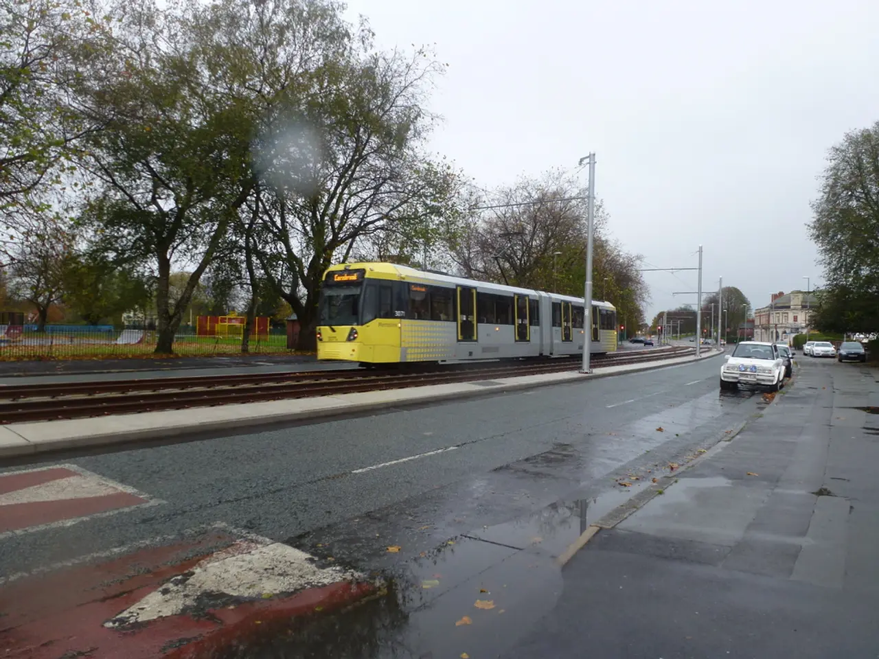 In this image there is road, there are vehicles on the road, there are buildingś, there are poleś,...