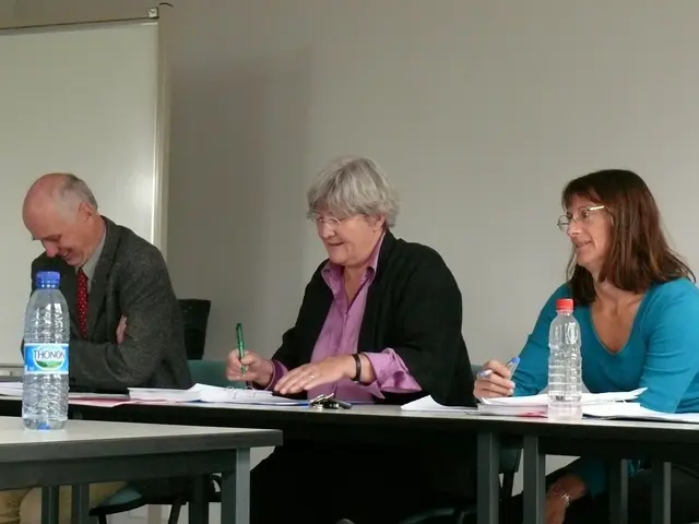 There are three members sitting in the chair in front of a table on which some papers, Water...