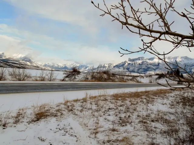There is a road and there is snow on either sides of it and there are mountains covered with snow...