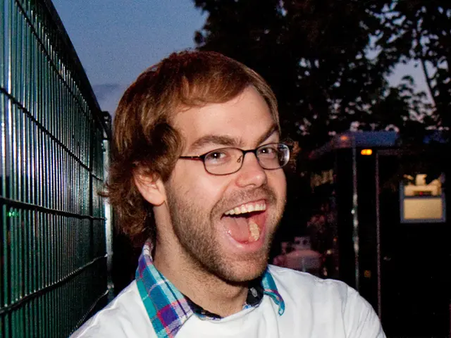 Here we can see a man posing to a camera. He has spectacles and he is smiling. In the background we...