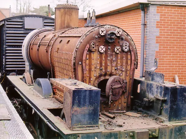 In the picture I can see a train. In the background I can see buildings, pipe attached to a brick...