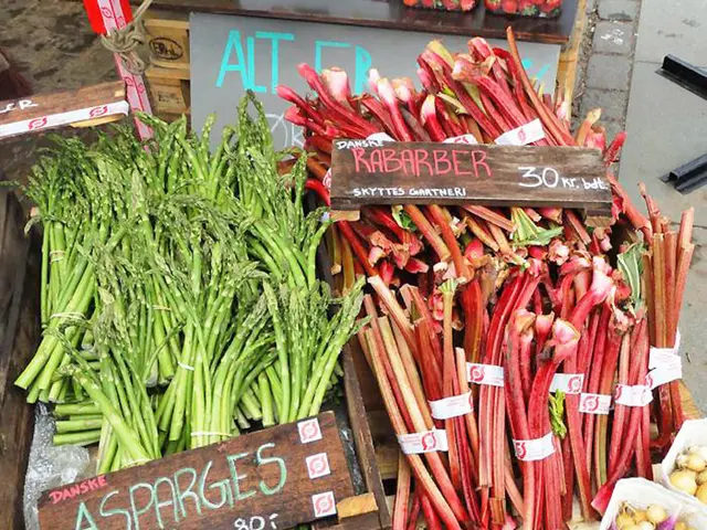 In the picture we can see a wooden plank on it we can see some leafy vegetables with price boards.