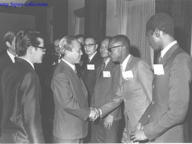 This is a black and white image where we can see men are standing. They are wearing suits. In the...